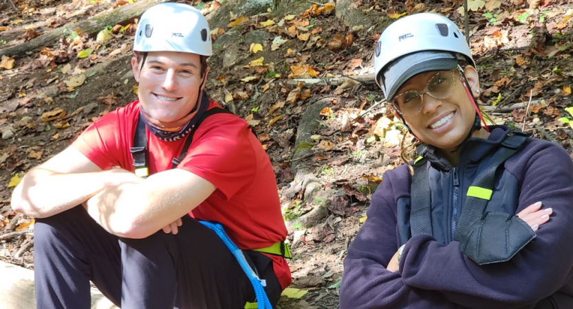 two people wearing helmets smile at the camera